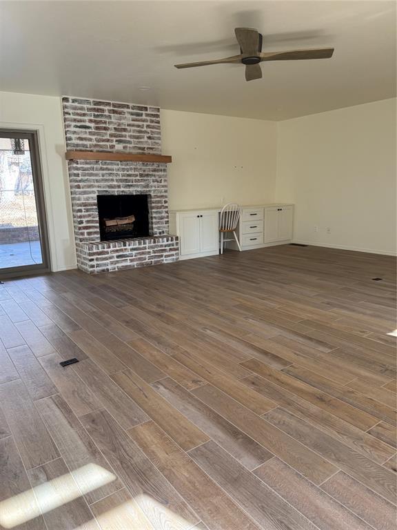 unfurnished living room with hardwood / wood-style flooring, ceiling fan, a fireplace, and built in desk