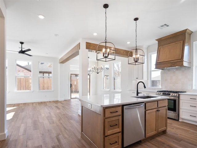 kitchen featuring premium range hood, sink, an island with sink, pendant lighting, and stainless steel appliances