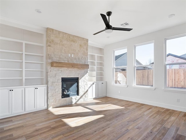 unfurnished living room with built in shelves, a healthy amount of sunlight, a fireplace, and light hardwood / wood-style floors