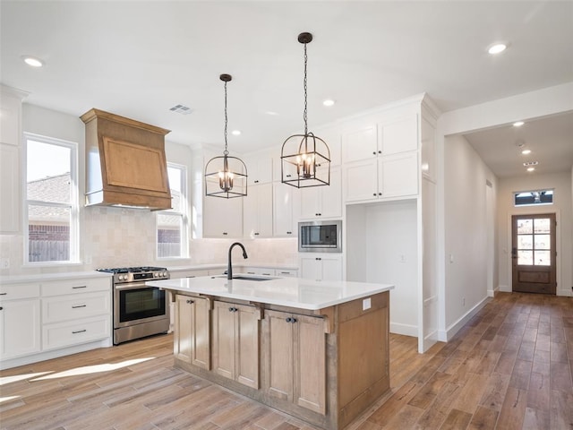 kitchen featuring appliances with stainless steel finishes, white cabinetry, an island with sink, sink, and hanging light fixtures