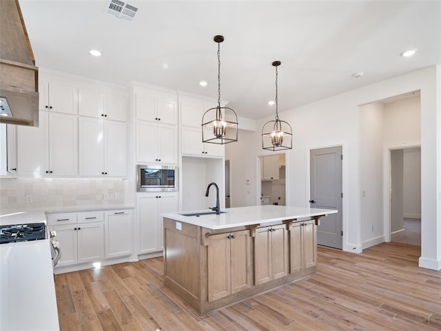 kitchen featuring pendant lighting, stainless steel microwave, white cabinetry, sink, and a kitchen island with sink