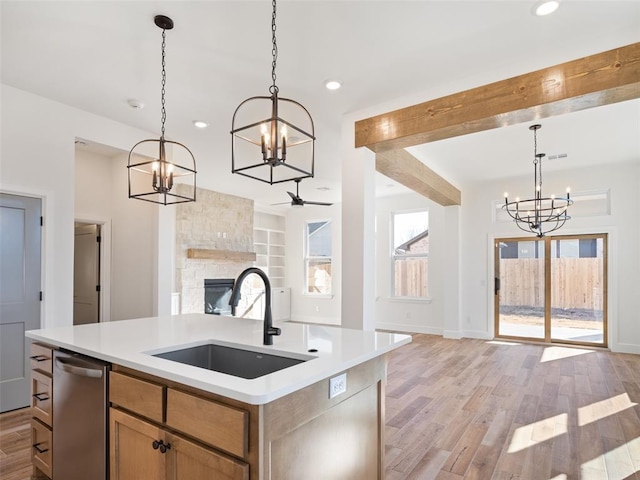 kitchen featuring pendant lighting, sink, an island with sink, a stone fireplace, and stainless steel dishwasher