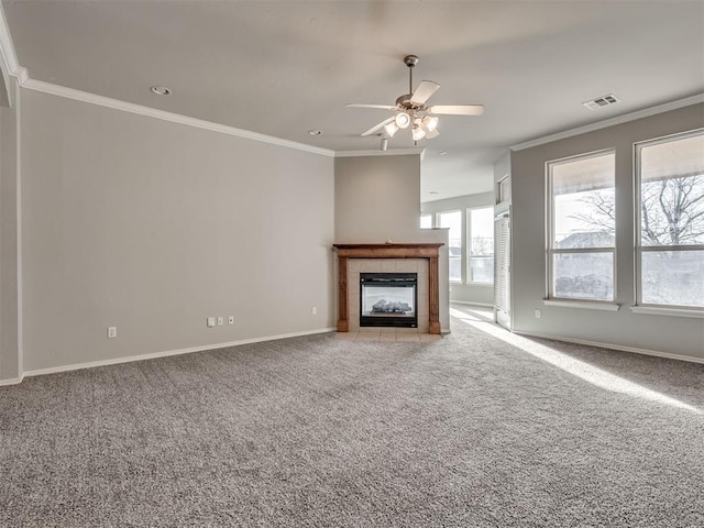 unfurnished living room featuring crown molding, ceiling fan, a tiled fireplace, and light carpet