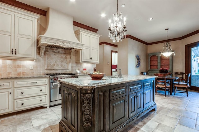 kitchen featuring a kitchen island with sink, custom range hood, high end stainless steel range, and decorative light fixtures