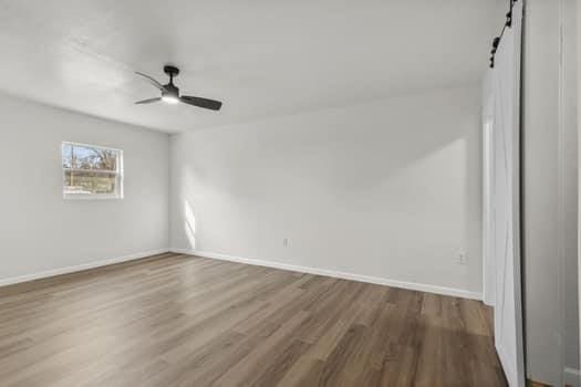 empty room with wood-type flooring, a barn door, and ceiling fan