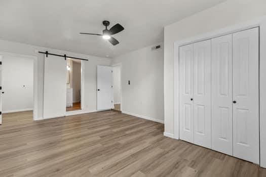 unfurnished bedroom with a barn door, ceiling fan, and light hardwood / wood-style flooring