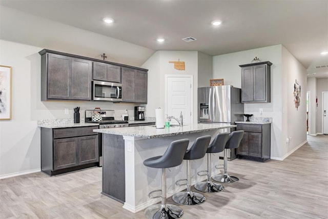 kitchen featuring appliances with stainless steel finishes, a breakfast bar, sink, a center island with sink, and light hardwood / wood-style flooring