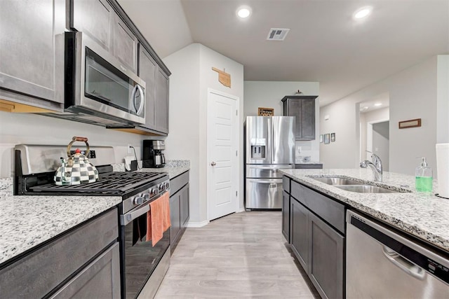 kitchen with light stone counters, stainless steel appliances, light hardwood / wood-style floors, and sink