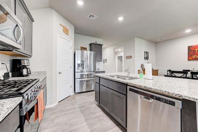 kitchen featuring light stone countertops, appliances with stainless steel finishes, sink, and light hardwood / wood-style flooring