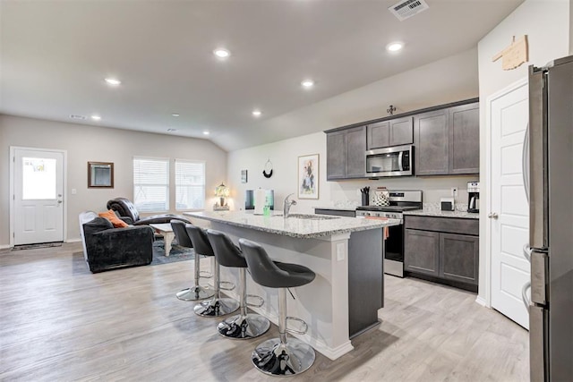 kitchen featuring appliances with stainless steel finishes, a breakfast bar, light stone countertops, a center island with sink, and light wood-type flooring