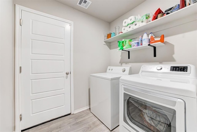 clothes washing area with washing machine and dryer and light wood-type flooring