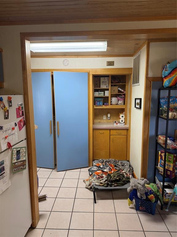 interior space with light tile patterned floors, light countertops, freestanding refrigerator, open shelves, and brown cabinetry