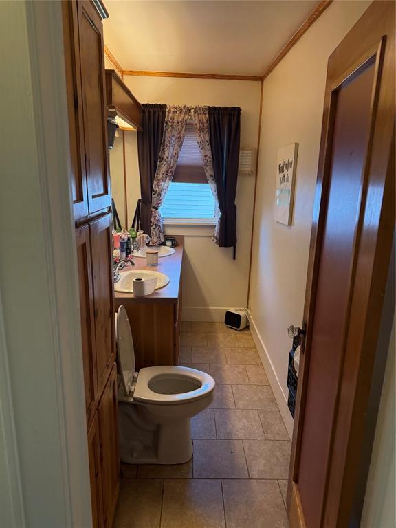 bathroom featuring tile patterned flooring, toilet, vanity, baseboards, and ornamental molding