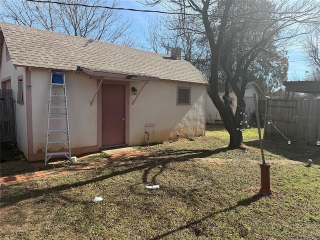 property entrance featuring stucco siding, roof with shingles, fence, and a lawn