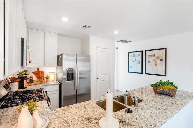 kitchen with stainless steel appliances, light stone countertops, white cabinets, and kitchen peninsula