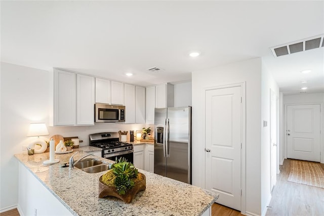 kitchen featuring stainless steel appliances, white cabinetry, sink, and light stone counters