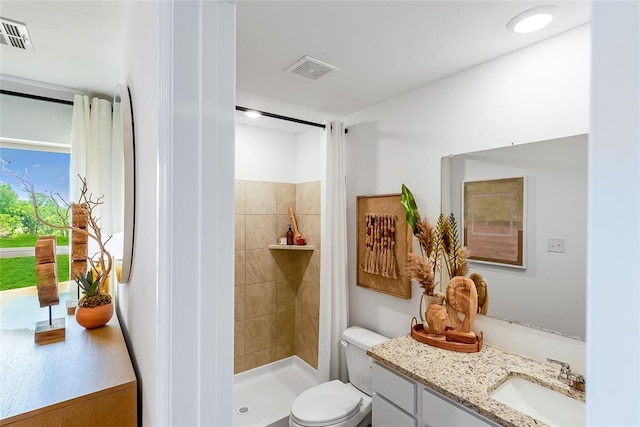 bathroom with tiled shower, vanity, and toilet