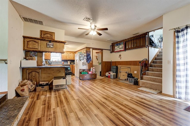 interior space featuring ceiling fan, light hardwood / wood-style flooring, a textured ceiling, and wood walls