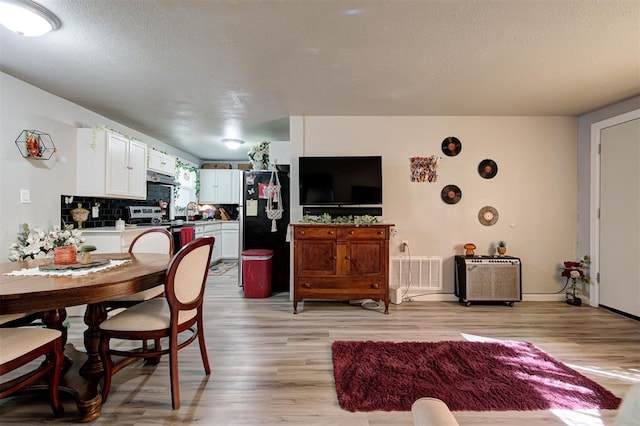 kitchen with light hardwood / wood-style flooring, white cabinetry, black refrigerator, tasteful backsplash, and stainless steel range with electric cooktop