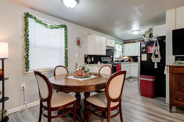 dining room with sink, a textured ceiling, and light wood-type flooring