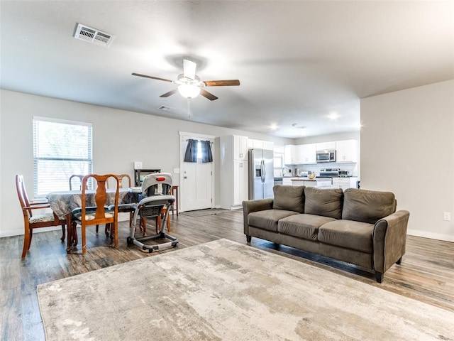 living area with light wood-style floors, visible vents, baseboards, and a ceiling fan