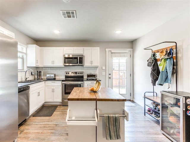 kitchen with beverage cooler, visible vents, white cabinets, stainless steel appliances, and backsplash