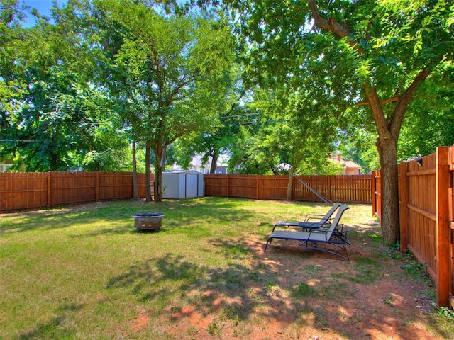 view of yard featuring a shed, a fire pit, a fenced backyard, and an outdoor structure