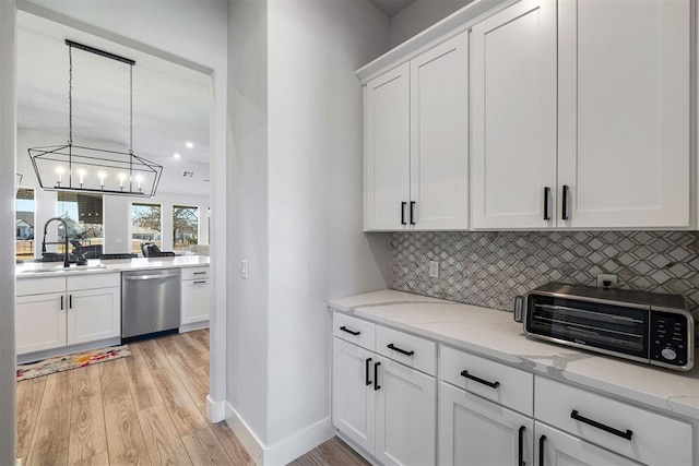 kitchen featuring pendant lighting, sink, white cabinets, decorative backsplash, and stainless steel dishwasher