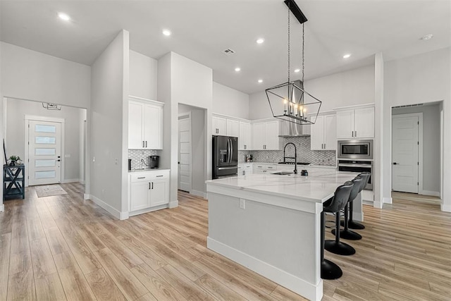 kitchen with stainless steel appliances, white cabinetry, light stone countertops, and a center island with sink