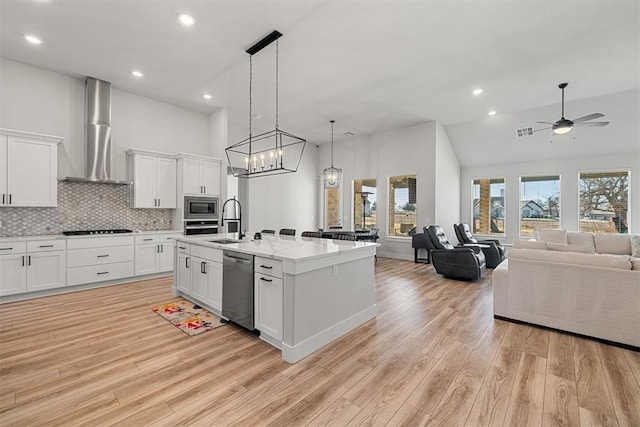 kitchen with sink, appliances with stainless steel finishes, white cabinetry, a center island with sink, and wall chimney exhaust hood