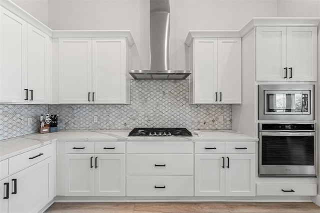 kitchen with stainless steel appliances, light stone countertops, white cabinets, decorative backsplash, and wall chimney exhaust hood