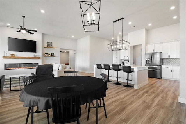 dining area with ceiling fan, a towering ceiling, sink, and light wood-type flooring