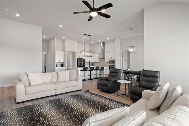 living room with ceiling fan with notable chandelier, light hardwood / wood-style floors, and a towering ceiling