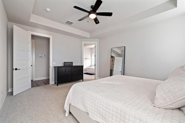 carpeted bedroom with ceiling fan and a tray ceiling