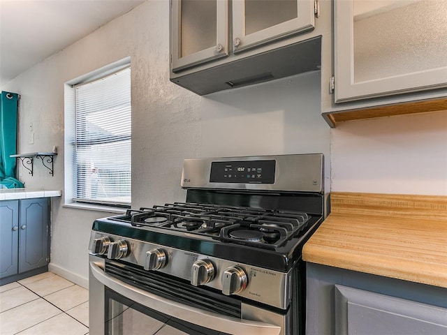 kitchen featuring wood counters, light tile patterned floors, stainless steel gas range oven, and gray cabinets