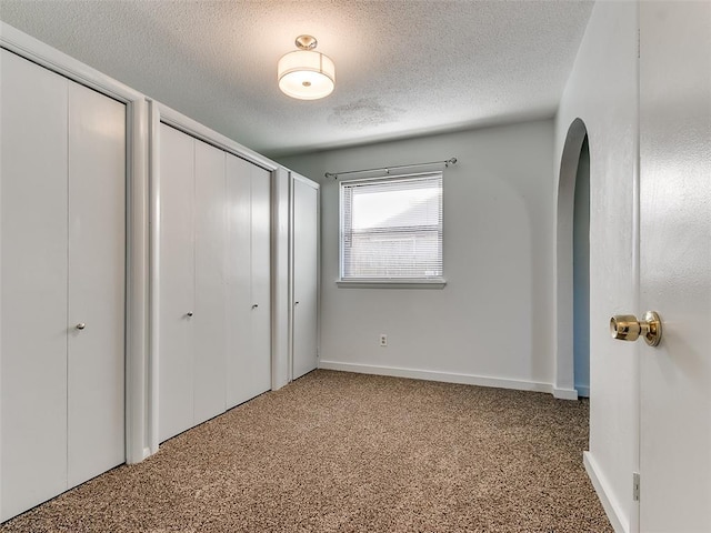 unfurnished bedroom with multiple closets, carpet floors, and a textured ceiling