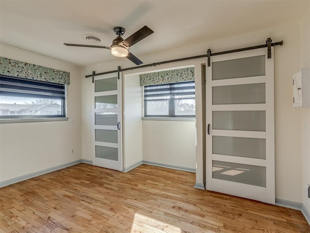 unfurnished bedroom with ceiling fan, a barn door, light hardwood / wood-style floors, and multiple windows