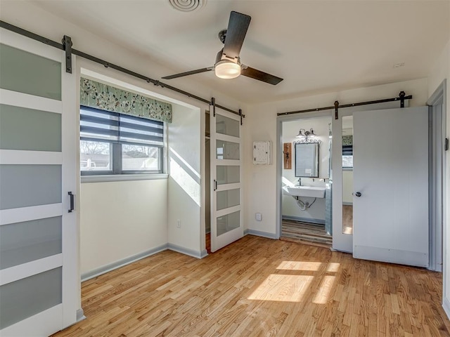 unfurnished bedroom with a barn door, ceiling fan, and light hardwood / wood-style flooring