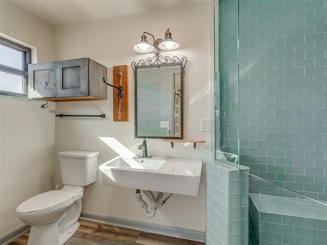 bathroom with wood-type flooring, tiled shower, sink, and toilet