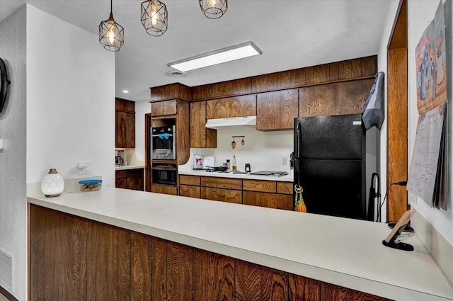 kitchen with black fridge, multiple ovens, white stovetop, and decorative light fixtures