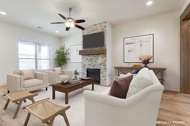 living room featuring a stone fireplace, ceiling fan, and light hardwood / wood-style flooring