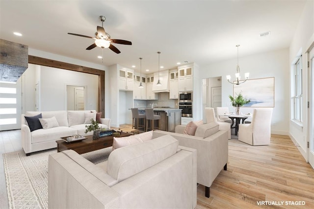 living room with ceiling fan with notable chandelier and light hardwood / wood-style flooring