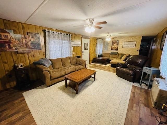 living room with dark wood-type flooring, ceiling fan, and wood walls