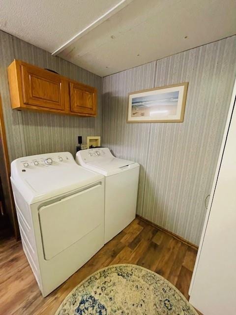 laundry room featuring cabinets, wood-type flooring, washing machine and clothes dryer, and a textured ceiling