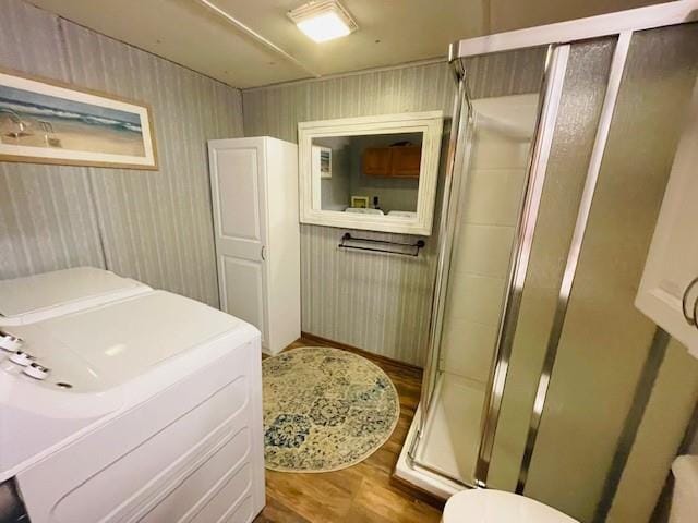 bathroom with washing machine and clothes dryer, toilet, a shower with shower door, and hardwood / wood-style floors