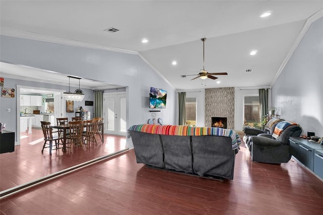 living room with a stone fireplace, dark hardwood / wood-style floors, lofted ceiling, ceiling fan, and crown molding