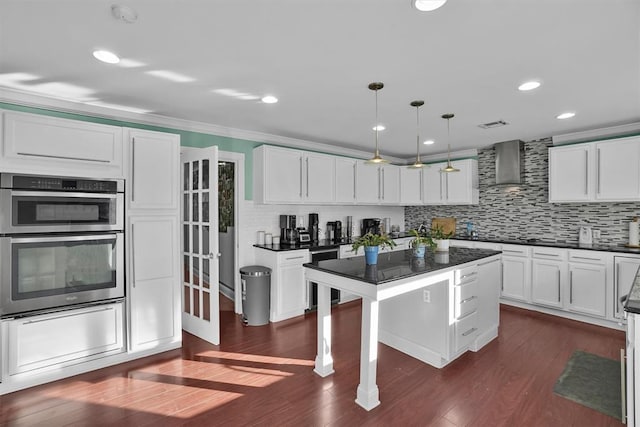 kitchen featuring white cabinets, dark hardwood / wood-style flooring, stainless steel double oven, hanging light fixtures, and wall chimney range hood