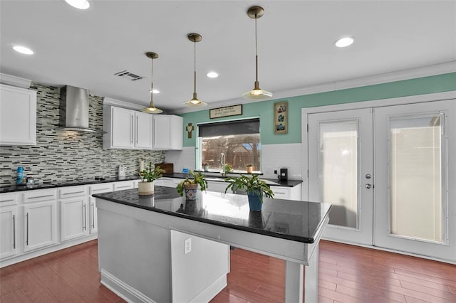 kitchen featuring a kitchen island, decorative light fixtures, white cabinets, wall chimney exhaust hood, and french doors