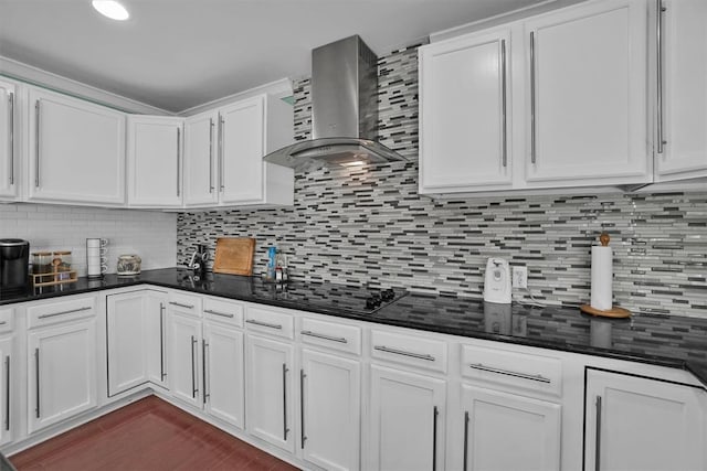 kitchen with white cabinets, black electric cooktop, decorative backsplash, dark stone counters, and wall chimney exhaust hood