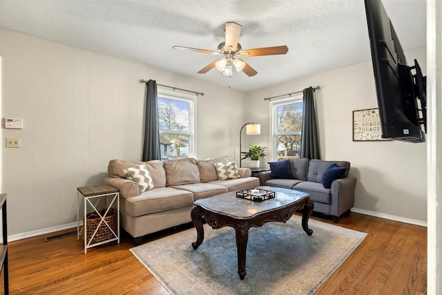 living room with a textured ceiling, wood finished floors, visible vents, baseboards, and a ceiling fan